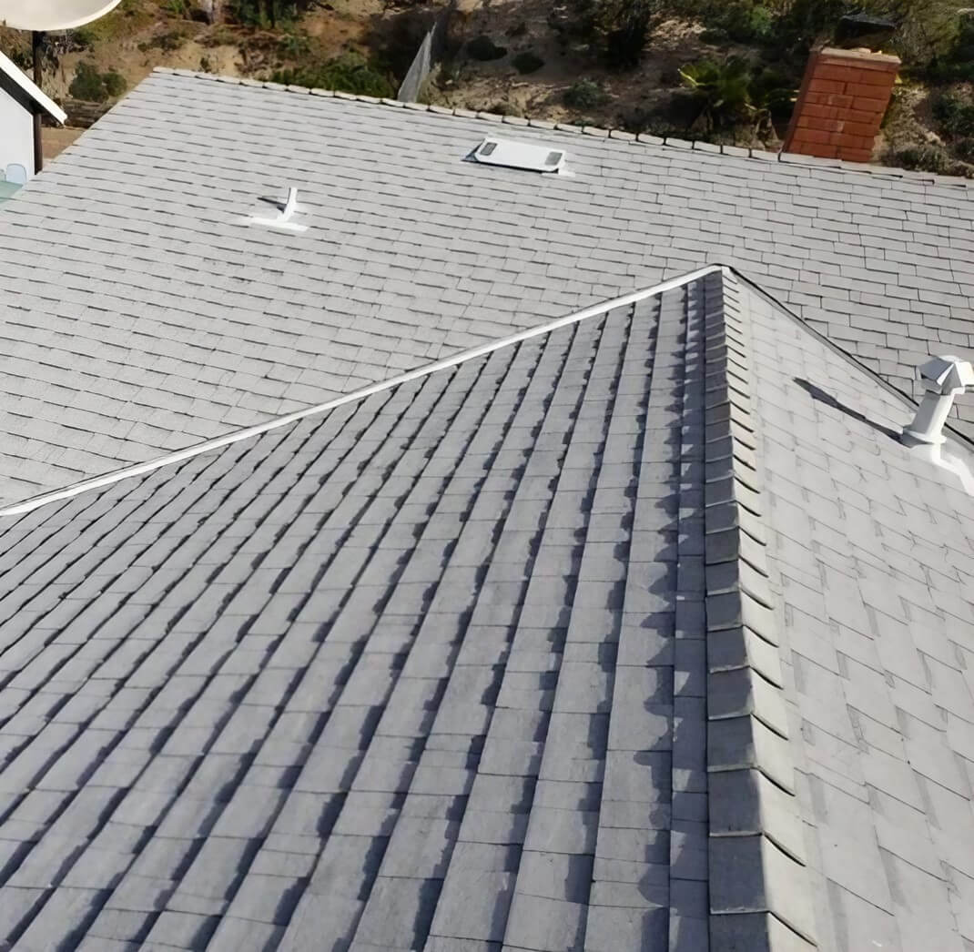 Aerial view of a grey shingle roof at an angle, showcasing the texture and pattern of the shingles against a natural landscape background.