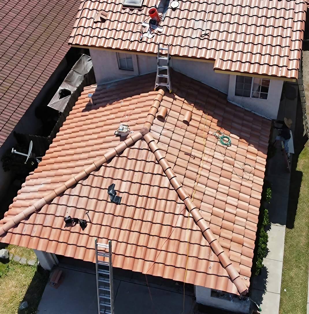 Aerial view of a home with terracotta tile roof, showing a roofer at work and two ladders positioned against the roof.